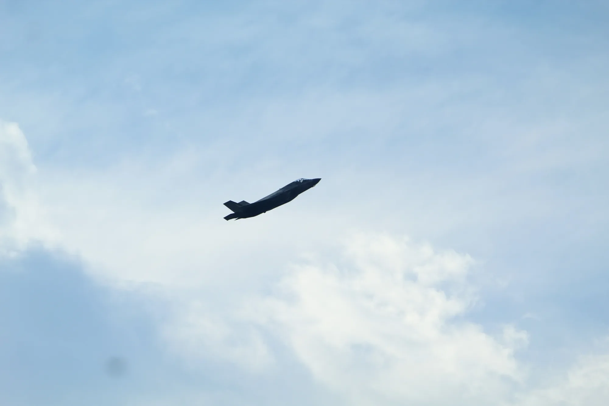 F-35 Lightning II climbing through a pale blue sky